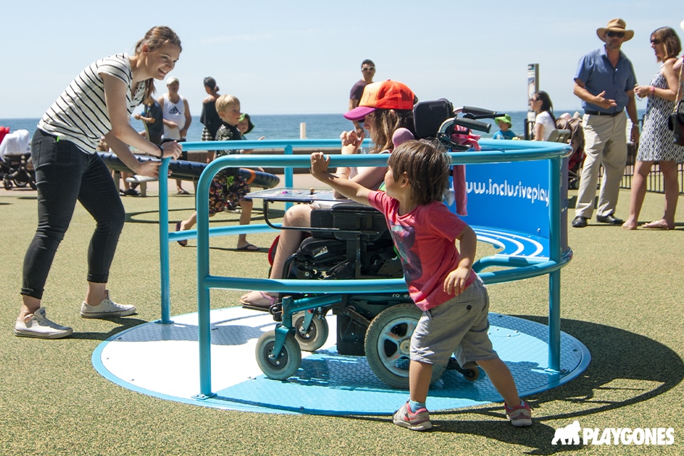 un enfant sur un fauteuil roulant joue sur un tourniquet inclusif