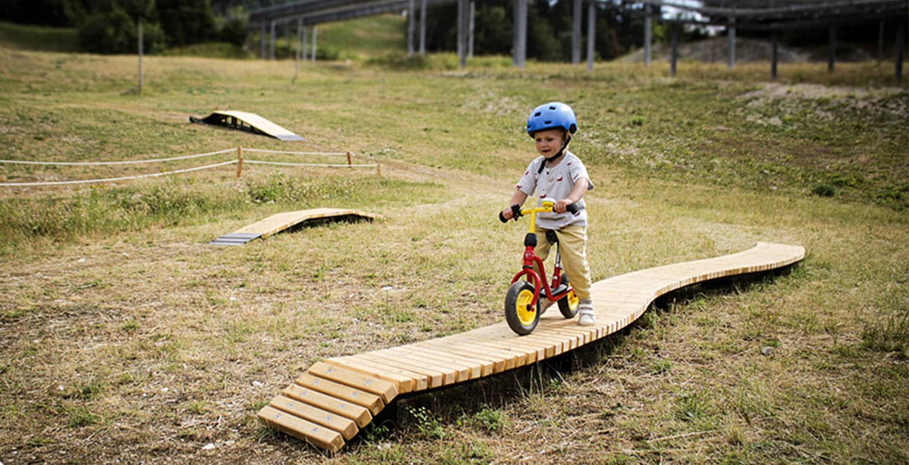 Enfant en draisienne sur un module d'initiation en bois en montagne