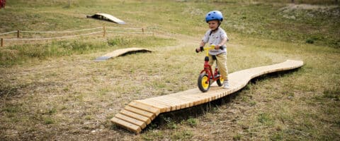 Jeune enfant en draisienne sur un parcours vélo en bois dans un espace vert