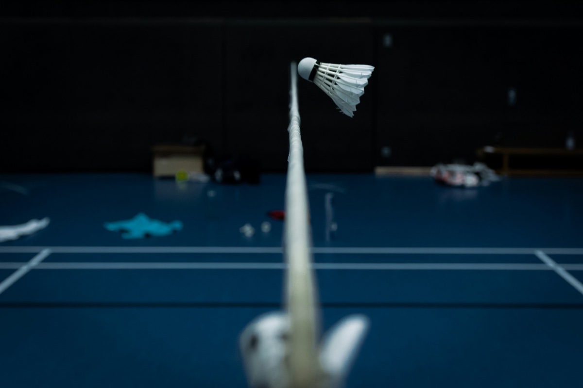 Volant et filet de badminton sur terrain réglementaire Gros plan sur un volant de badminton posé sur le filet réglementaire, terrain bleu avec lignes de marquage en arrière-plan