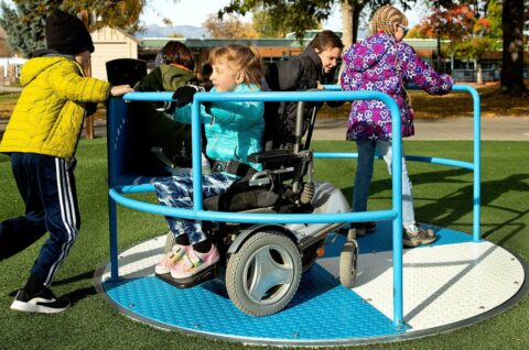 Petite fille en fauteuil roulant sur un tourniquet inclusif poussée par d'autres enfants