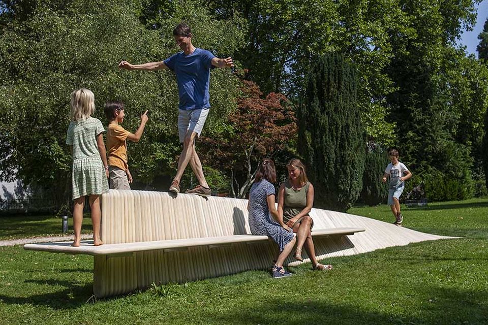 Banc sculpture MoveArt en bois, famille jouant dans un parc