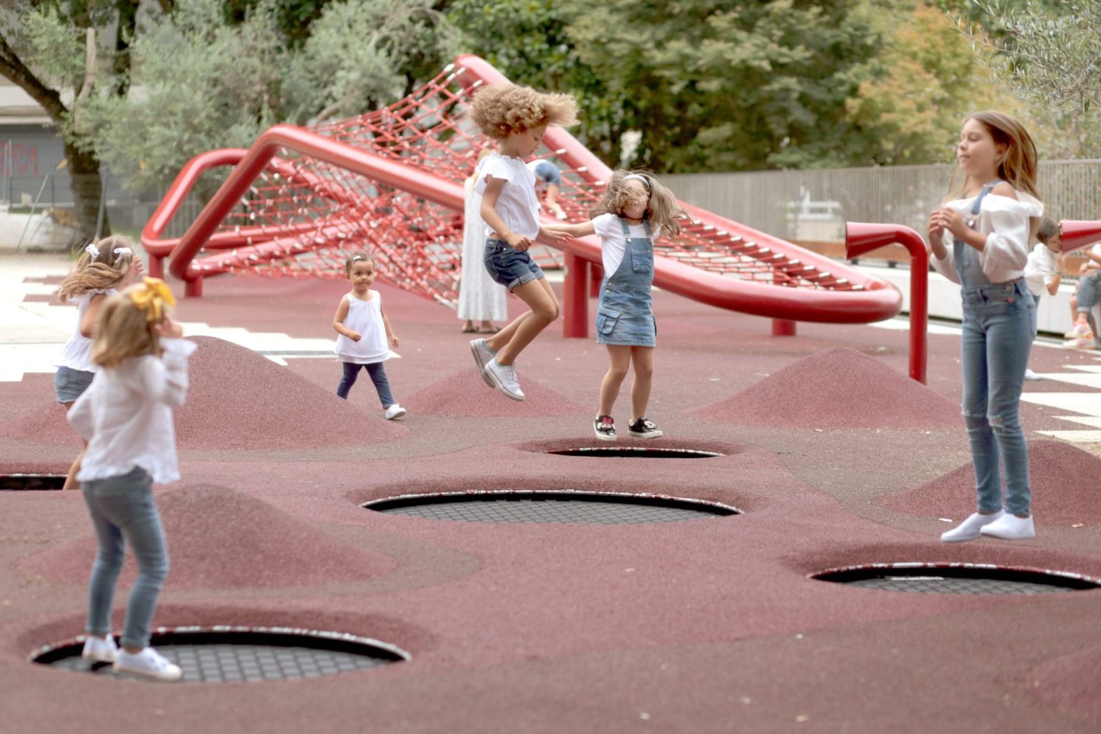 Enfants jouant sur un grand filet de grimpe rouge et des trampolines enterrés Galopin