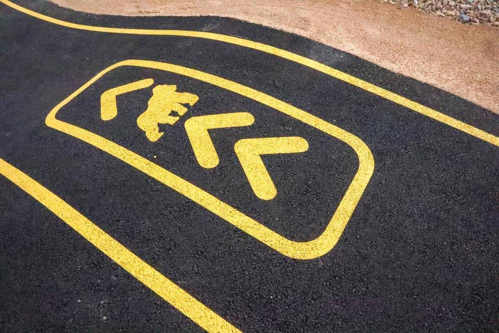 Pictogramme de sens de circulation et lignes de rive peints en jaune sur l'enrobé d'un pumptrack