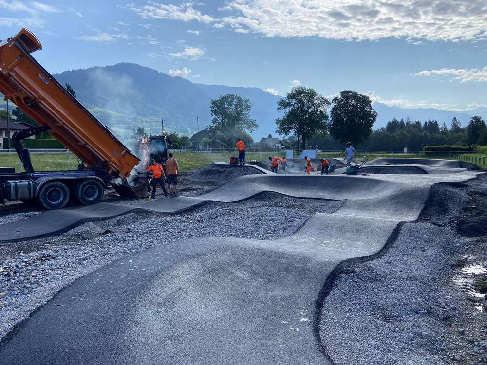 Camion déversant l'enrobé sur les bosses modelées d'un pumptrack, équipes Playgones au travail en montagne