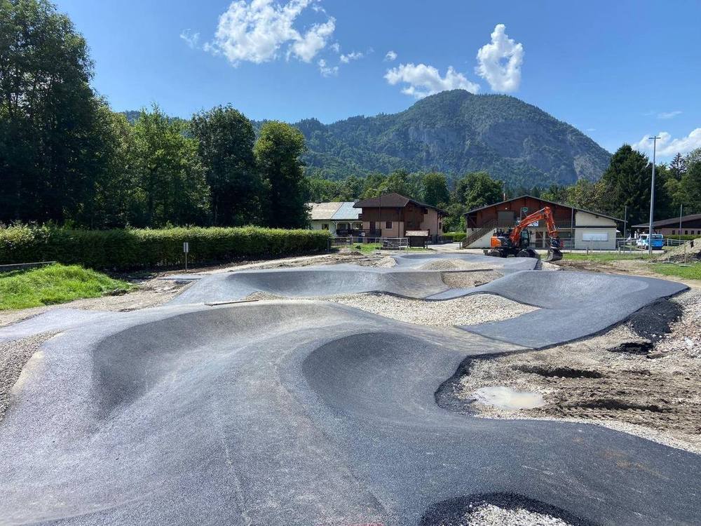 Pumptrack en enrobé fraîchement revêtu en fin de chantier : enchaînement de bosses et virages relevés face aux montagnes