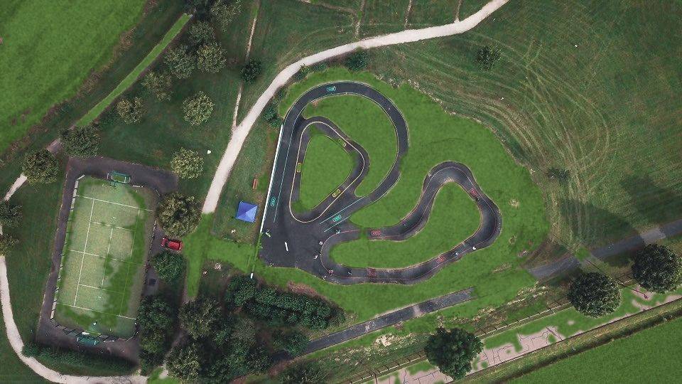 Vue aérienne du tracé d'un pumptrack en enrobé en double boucle à côté d'un court de tennis, entouré de pelouse