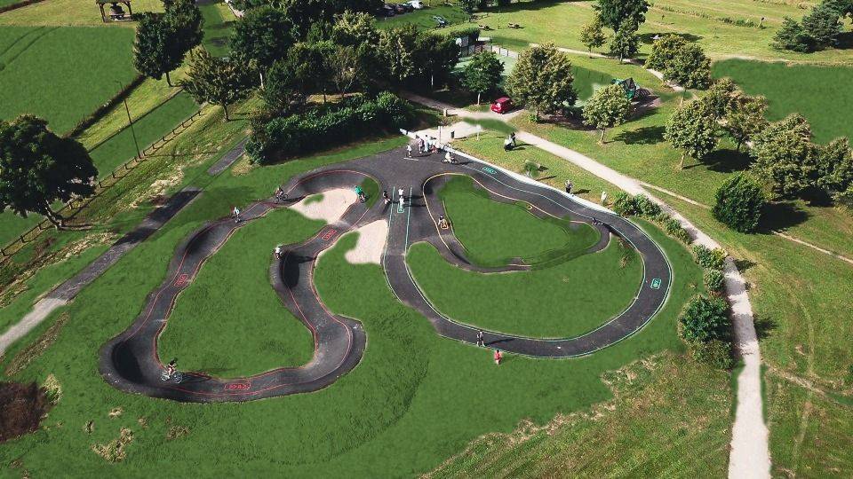 Vue de drone d'un pumptrack en enrobé à deux boucles intégré dans un parc engazonné, réalisation Playgones