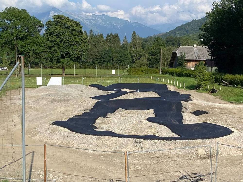 Chantier de pumptrack en enrobé : terrassement, plateforme granulaire et premières formes revêtues, clôture de chantier