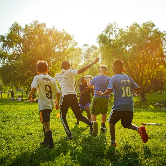 Des enfants courent après un ballon dans l'herbe, au soleil